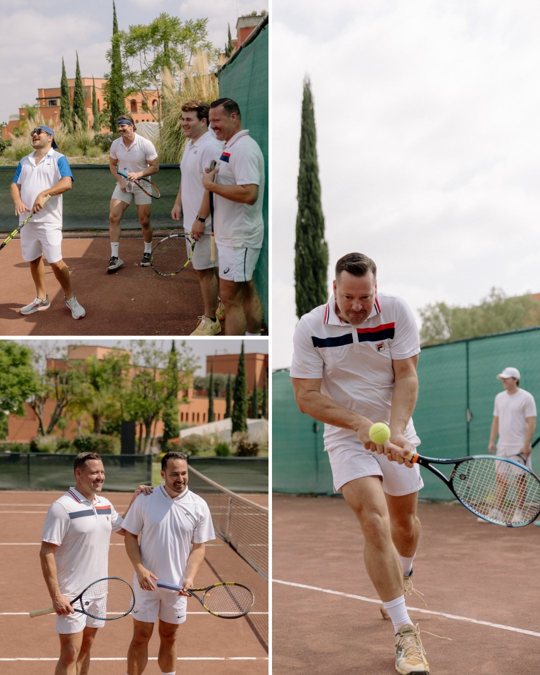 Three men in white tennis outfits are talking and playing on an outdoor tennis court with trees and buildings in the background.