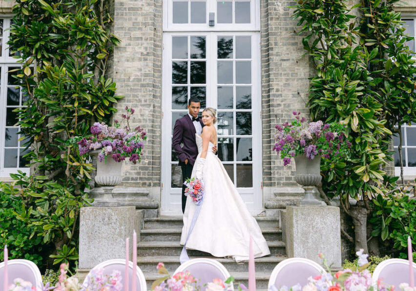 bride and groom pose on steps near window with table in foreground