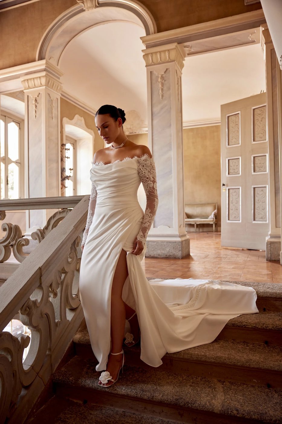 Model wearing Jessa dress by Justin Alexander walks downstairs in a grand, historic home.