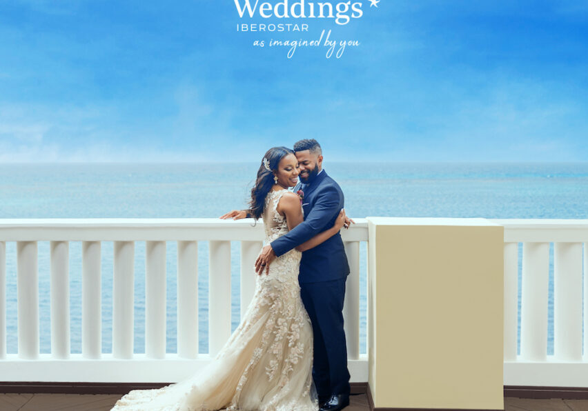 bride and groom hug on terrace overlooking the Caribbean Sea with the Iberostar Weddings logo